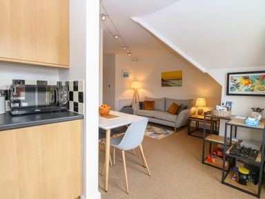 An open plan living room and kitchen area with a microwave on the kitchen counter dining table with chairs and a grey sofa with cushions in the living area at Flat 3 Cromer