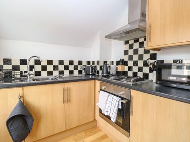 A kitchen with wooden cabinets black and white checkered backsplash black countertop and stainless steel appliances at Flat 3 in Cromer