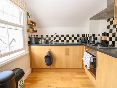 A kitchen with wooden cabinets black countertop black and white checkered backsplash and window at Flat 3 in Cromer