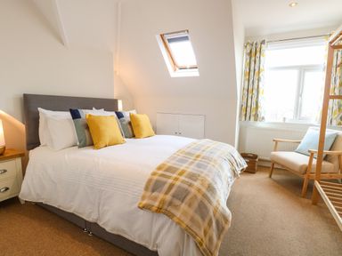 A bedroom with a bed with pillows and blanket a chair a window and a skylight at Flat 3 in Cromer