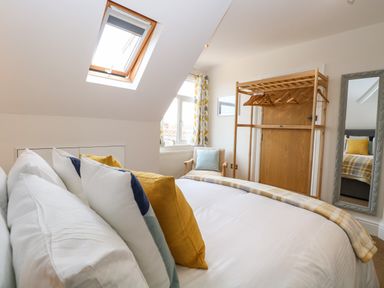 A bedroom with a bed with pillows skylight window chair wooden clothes rack and wall mirror at Flat 3 in Cromer