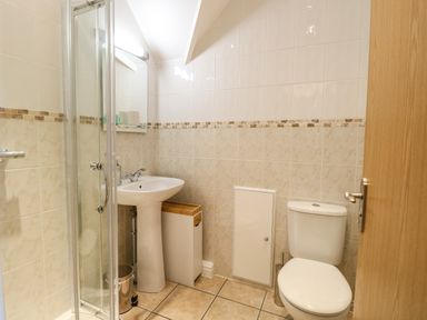 A bathroom with a shower, sink, toilet, mirror, and storage cabinet at Flat 3 in Cromer