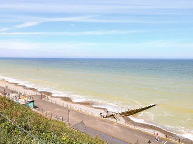 A seafront with a paved promenade and a wooden groyne extending into the sea at Flat 3 in Cromer