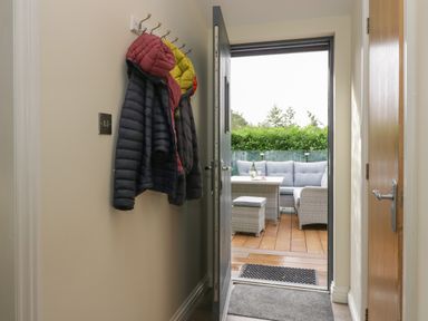 A hallway with coats hanging on hooks and a door open to a deck with outdoor seating at Bay Tree Lodge in Cartmel