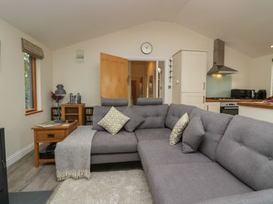 A living room with a gray sofa and pillows next to a wooden side table and an open door at Bay Tree Lodge in Cartmel