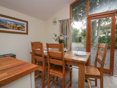 A dining area with a wooden table and chairs set for four with flowers and wine outside the window at Bay Tree Lodge in Cartmel