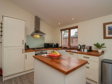 A kitchen with wooden countertops a kitchen island a stove microwave and window blinds at Bay Tree Lodge in Cartmel