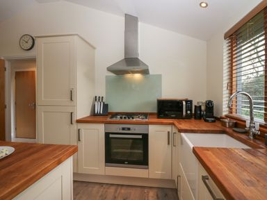 A kitchen with wooden countertops gas stove knives microwave coffee machine and a sink at Bay Tree Lodge in Cartmel