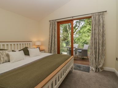 A bedroom with a bed a lamp and a door opening to an outdoor seating area at Bay Tree Lodge in Cartmel