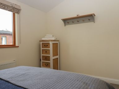 A bedroom corner with a small chest of drawers topped with towels and a wall-mounted coat rack at Bay Tree Lodge in Cartmel