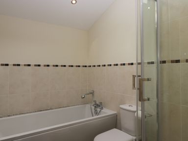 A bathroom with a bathtub a toilet and a glass shower enclosure at Bay Tree Lodge in Cartmel
