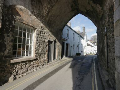 A street view through a stone archway with white houses and a narrow road at Bay Tree Lodge in Cartmel