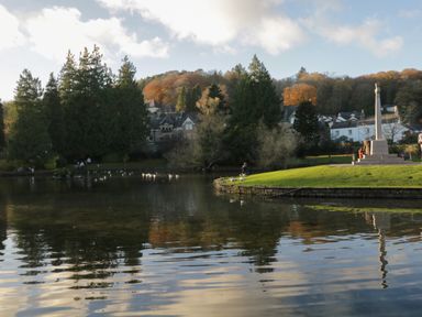 A pond with birds and a monument near houses and trees at Bay Tree Lodge in Cartmel