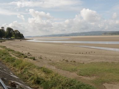 A sandy beach with patches of grass and water under a cloudy sky at Bay Tree Lodge in Cartmel