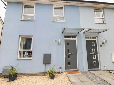The front of a blue house with two doors and four windows with plants in pots and welcome mat on one door at Ty Glas in Ogmore-by-Sea near St Brides Major