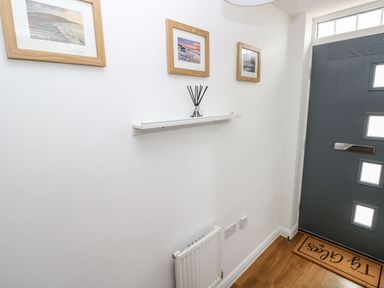 An entryway with a dark gray door a white wall with three framed pictures a small shelf with a reed diffuser a radiator and a doormat at Ty Glas in Ogmore-by-Sea near St Brides Major