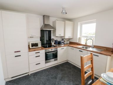A kitchen with white cabinets wooden countertops a built-in oven stove a toaster a kettle a stainless steel sink and a wooden chair at Ty Glas in Ogmore-by-Sea near St Brides Major