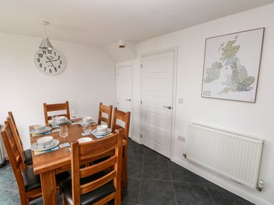 A dining room with a wooden table set for six with plates and glasses a wall clock and a framed map above a radiator at Ty Glas in Ogmore-by-Sea near St Brides Major