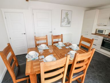 A dining table set with plates bowls glasses and cutlery in a kitchen with wooden chairs and white cabinets at Ty Glas Ogmore-by-Sea near St Brides Major