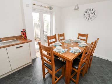 A dining area with a wooden table set for six and a kitchen sink to the side at Ty Glas in Ogmore-by-Sea near St Brides Major