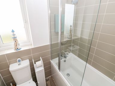 A bathroom with a toilet a bathtub with glass shower screen and a lighthouse decoration on the window ledge at Ty Glas in Ogmore-by-Sea near St Brides Major