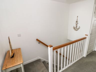 A staircase with wooden handrails and white balusters with a small table holding a decorative sailboat and an anchor decoration on the wall at Ty Glas in Ogmore-by-Sea near St Brides Major