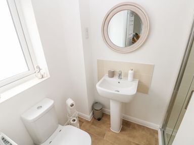 A bathroom with a toilet a pedestal sink a round mirror and a shower at Ty Glas in Ogmore-by-Sea near St Brides Major