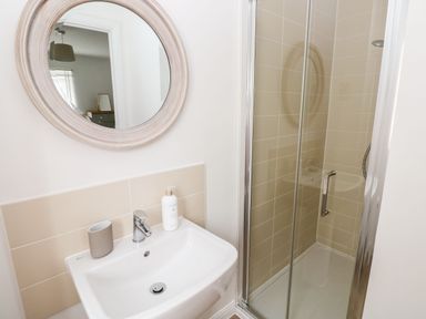 A bathroom with a white sink, a round mirror, a toothbrush holder, and a shower enclosure with glass doors at Ty Glas in Ogmore-by-Sea near St Brides Major