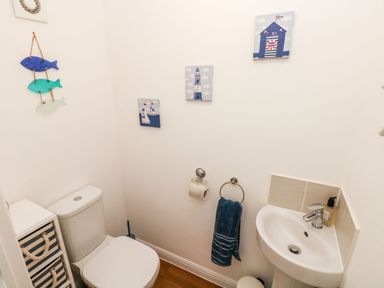 A small bathroom with a toilet a sink a blue towel on a ring and nautical-themed wall decorations at Ty Glas in Ogmore-by-Sea near St Brides Major