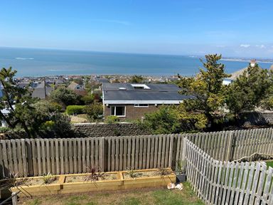 A backyard with a wooden fence and planter boxes with plants overlooking houses and the sea at Ty Glas in Ogmore-by-Sea near St Brides Major
