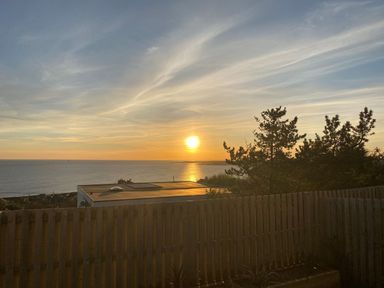 A sunset over the ocean with a wooden fence and trees in the foreground at Ty Glas in Ogmore-by-Sea near St Brides Major