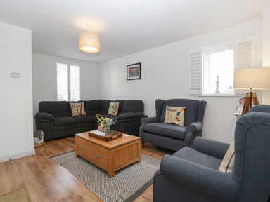 A living room with blue sofas a wooden coffee table and a lamp at Ty Glas in Ogmore-by-Sea near St Brides Major