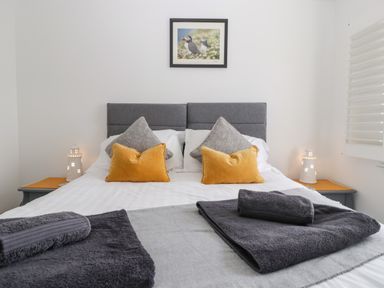 A bedroom with a double bed with gray and yellow pillows and gray towels on the bed at Ty Glas in Ogmore-by-Sea near St Brides Major