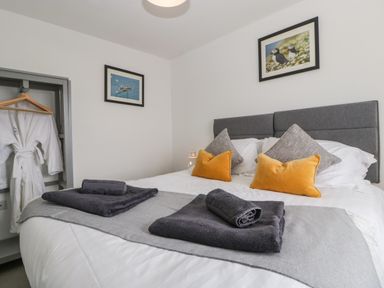 A bedroom with a double bed with pillows and folded towels and robes hanging in an open closet at Ty Glas in Ogmore-by-Sea near St Brides Major