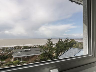 A window view overlooking houses trees and the sea on a cloudy day at Ty Glas in Ogmore-by-Sea near St Brides Major
