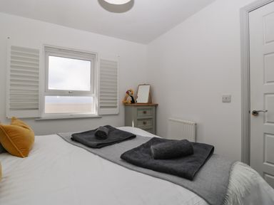 A bedroom with a bed with towels on it a window with shutters a small dresser with a mirror and a toy at Ty Glas Ogmore-by-Sea near St Brides Major