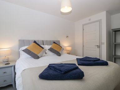 A bedroom with a bed with two pillows and folded towels on it with bedside tables and lamps at Ty Glas in Ogmore-by-Sea near St Brides Major