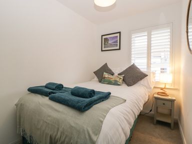 A bedroom with a double bed with pillows and towels and a bedside table with a lamp at Ty Glas in Ogmore-by-Sea near St Brides Major