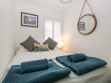 A bedroom with a bed covered with white sheets blue towels and pillows a round mirror and a framed picture on the walls at Ty Glas in Ogmore-by-Sea near St Brides Major