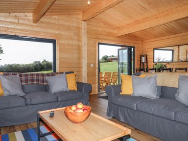 A living room with grey sofas and a wooden coffee table with a bowl of apples at Bluebell Lodge in Hittisleigh