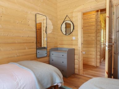 A bedroom with wooden walls two mirrors a gray chest of drawers and a bed with a light blanket at Bluebell Lodge in Hittisleigh