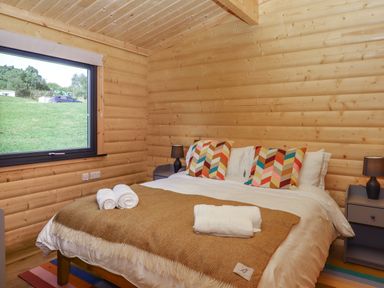 A bedroom with a bed with colorful pillows and a brown blanket next to a window at Bluebell Lodge in Hittisleigh