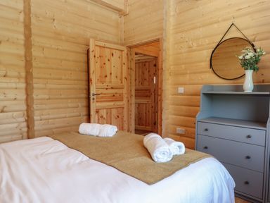 A bedroom with a bed with towels and a beige runner a grey dresser with a round mirror and flowers at Bluebell Lodge in Hittisleigh