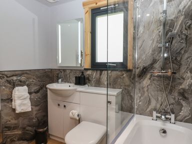A bathroom with a sink cabinet toilet bathtub with shower and a window at Bluebell Lodge in Hittisleigh