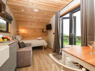 A wooden cabin interior with a bed sofa kitchen area dining table and glass doors leading outside at Orchard in Dalton-In-Furness