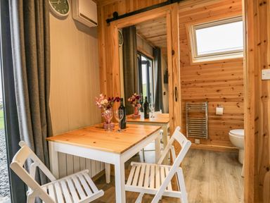 A small dining table with two white chairs flowers and wine bottles next to a bathroom with wooden walls at Orchard in Dalton-In-Furness