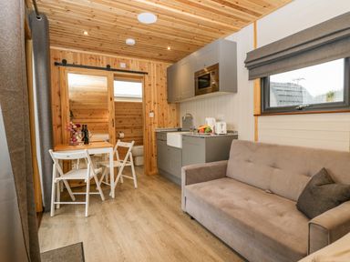 A small living area with a gray sofa, kitchenette with gray cabinets, dining table with two white chairs and wooden walls at Orchard Dalton-In-Furness