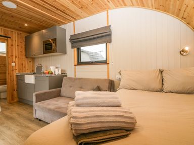 A bedroom with folded towels on the bed and a small kitchen and sofa in the background at Orchard in Dalton-In-Furness