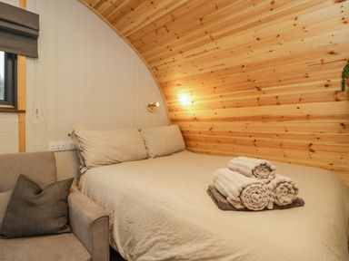 A bedroom with a bed with pillows and rolled towels and a chair with a cushion at Orchard in Dalton-In-Furness