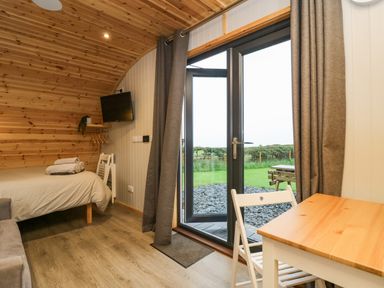 A room with a bed a wall-mounted TV a table with a chair and glass doors leading to a garden at Orchard in Dalton-In-Furness